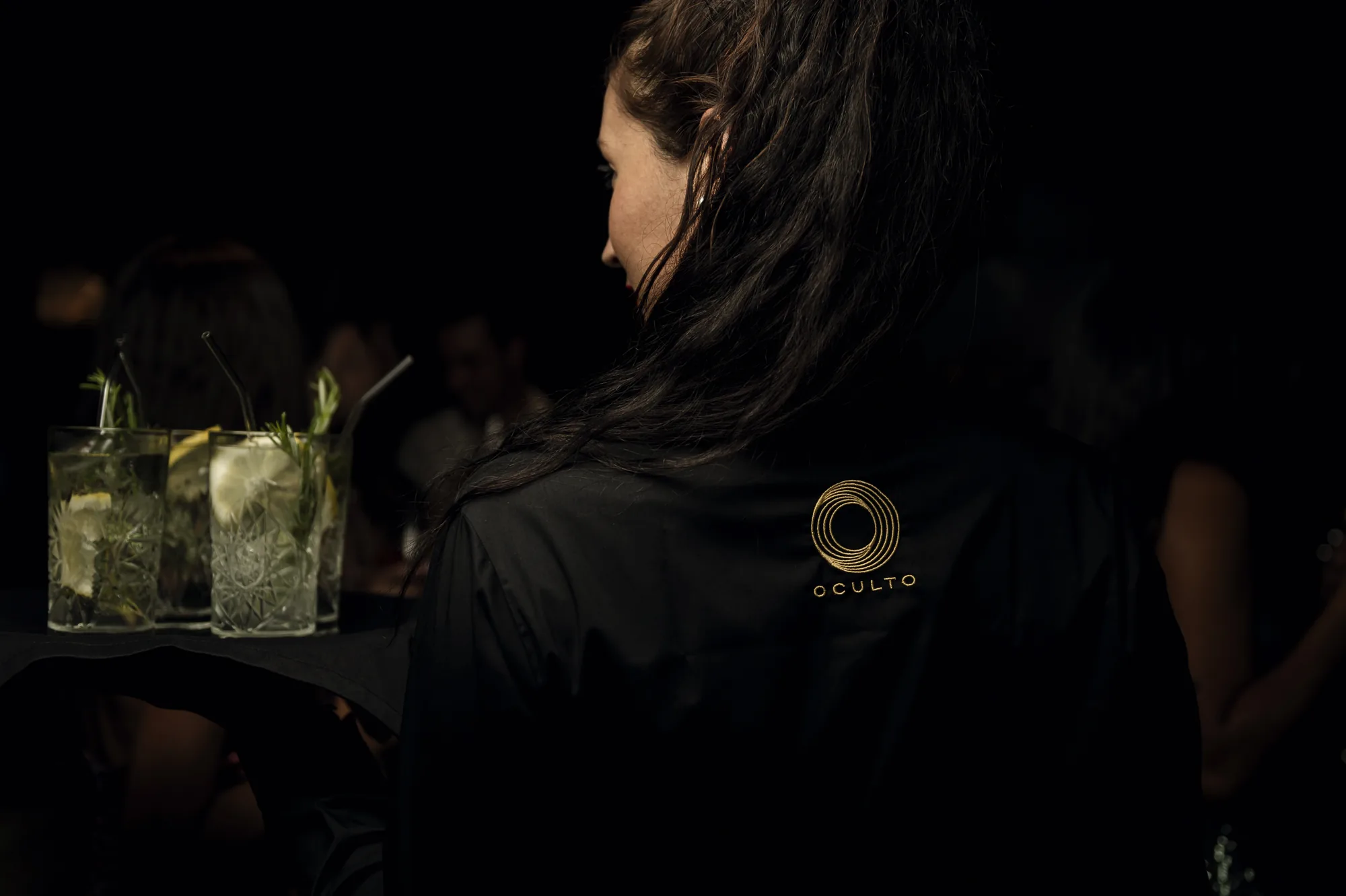 Camarera llevando una bandeja de mojitos por la sala del restaurante Oculto